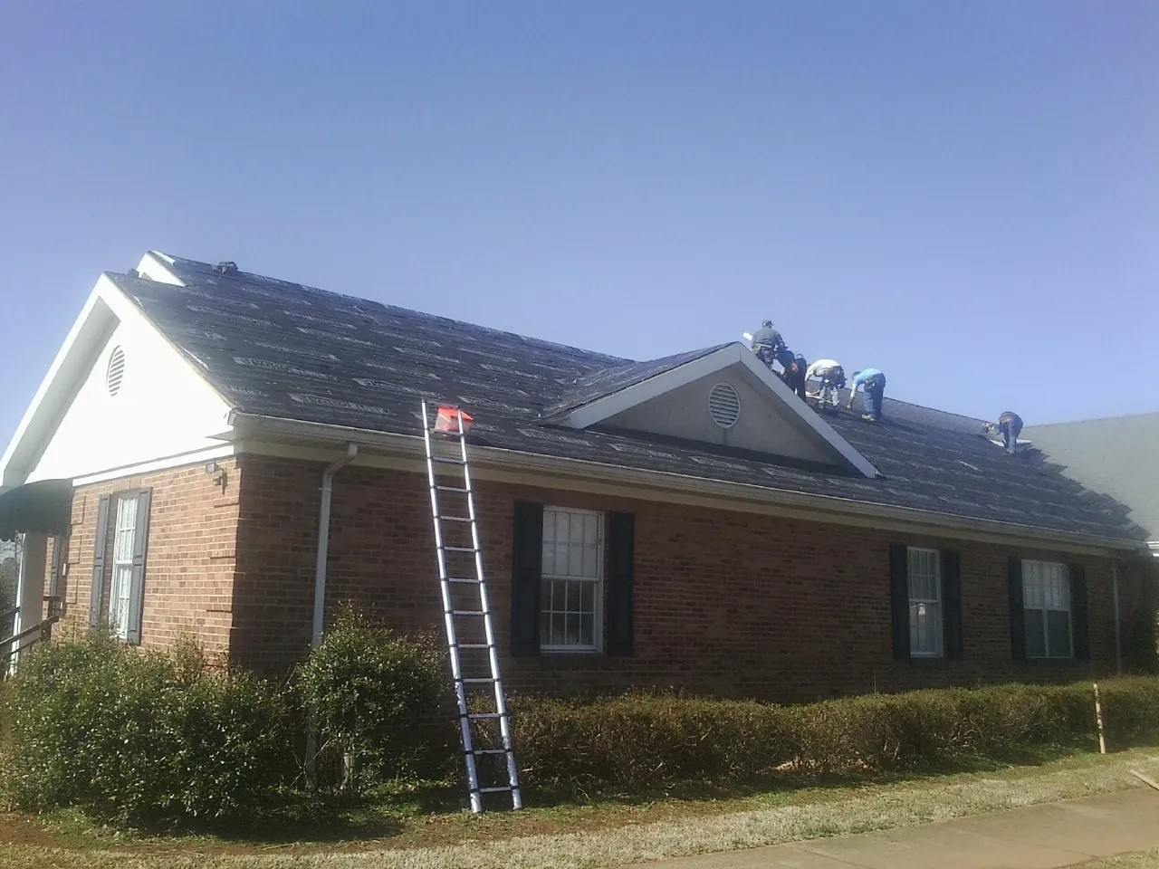 Crew tearing shingles off a brick ranch roof with a ladder set — Emergency Roof Repair work by our crew in Bardstown