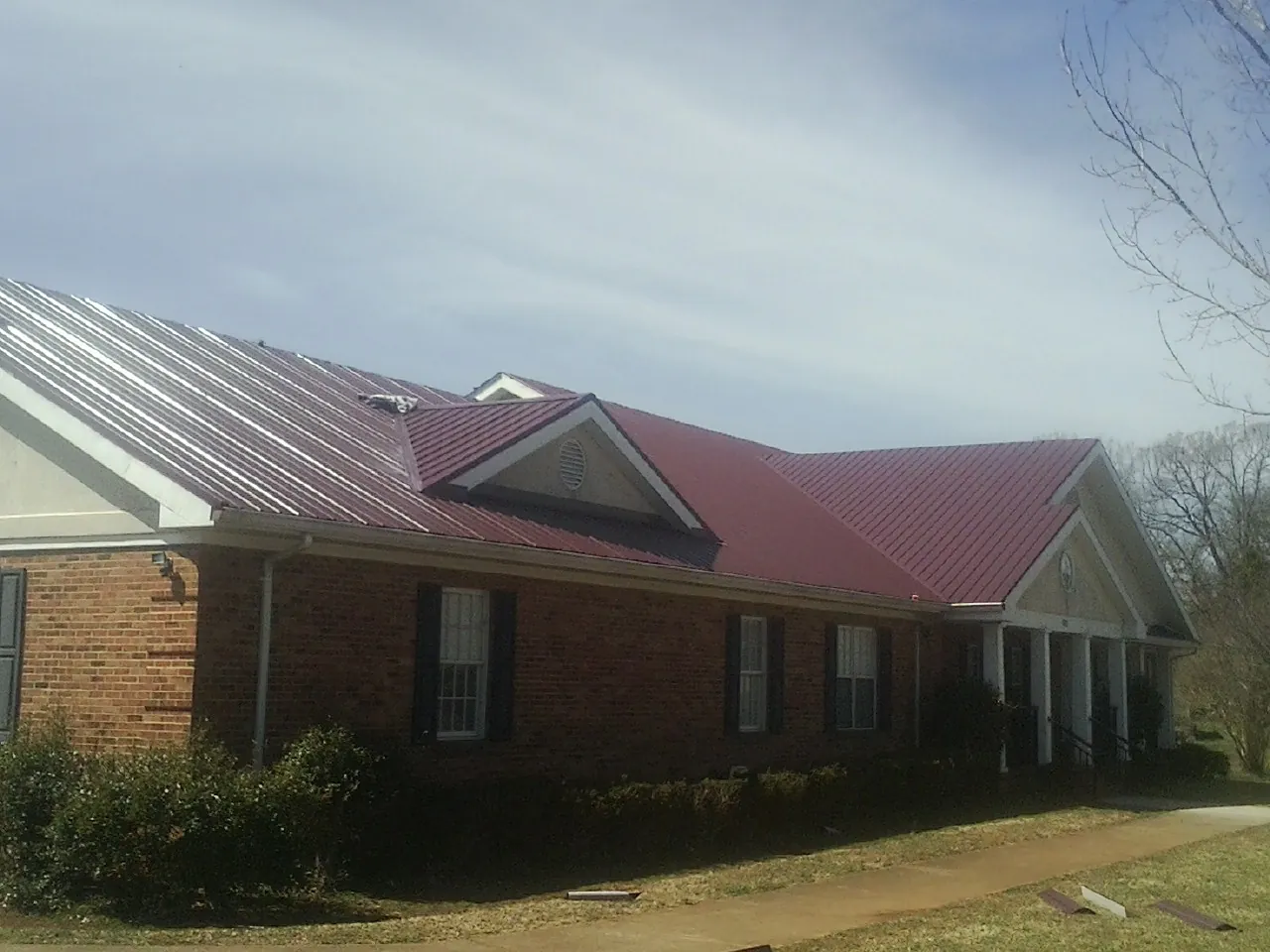 Red metal roof with gabled entries on a long brick building, from a Hail Damage Roof Repair job in Bardstown