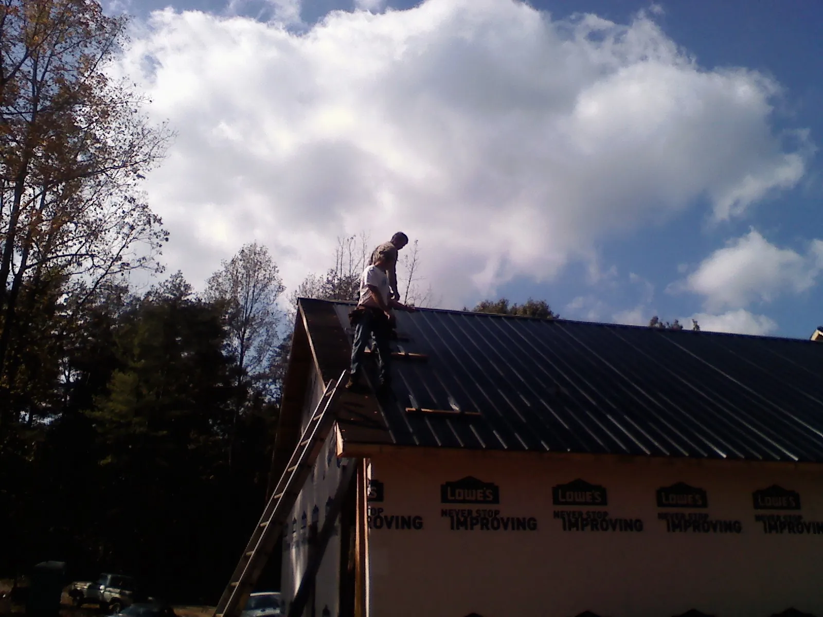 Roofer fastening dark metal panels high against a cloudy sky, from a Roof Inspection job in Bardstown